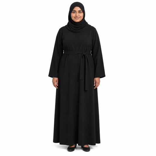 Model in a black hijab wearing a black full-length loose abaya with a matching black tie belt at the waist, on a white background