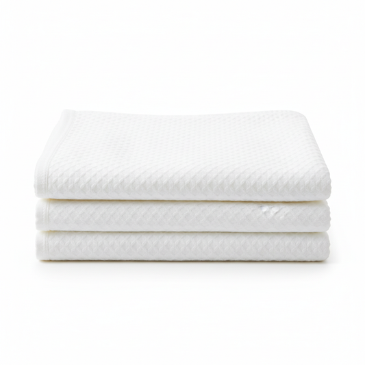 White hotel thermal blanket neatly folded into precise rectangular stack showing woven fabric texture and blanket weight on white background, commercial hospitality guestroom extra warmth layer