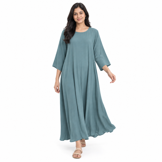 Full-body model wearing a dusty teal loose kaftan dress with flowing hem and three-quarter sleeves against white