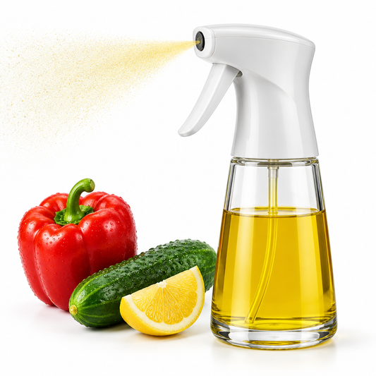 Refillable glass cooking oil sprayer bottle emitting fine oil mist beside fresh vegetables on pure white background