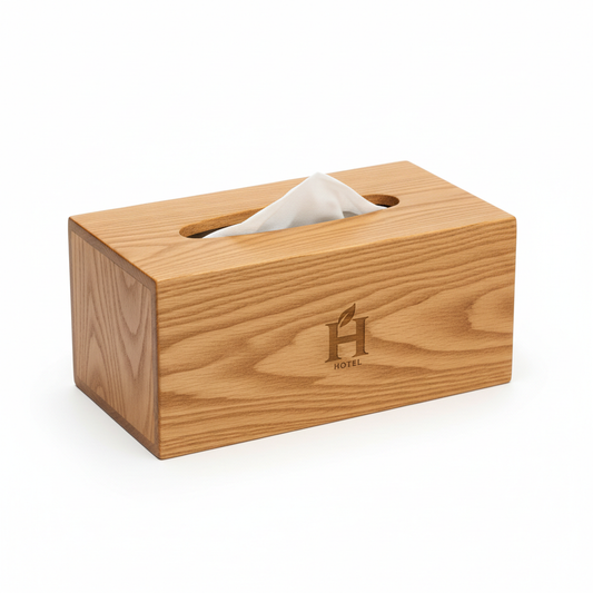 Warm honey oak wood hotel tissue box cover with top-opening slot showing tissue paper edge pulled through and laser-engraved hotel logo on front face with natural wood grain on white background, custom hospitality guestroom coordinated tissue holder