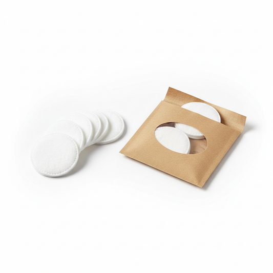Hotel cotton pads in kraft paper individual pack with clear window, pack open with round white cotton pads fanned out beside it on white background, guest vanity bathroom amenity
