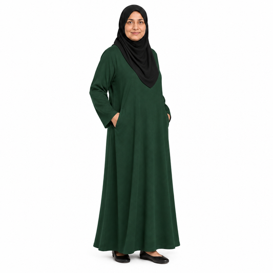 Angled full-length view of a dark green loose abaya with both hands in the side pockets, on a white background