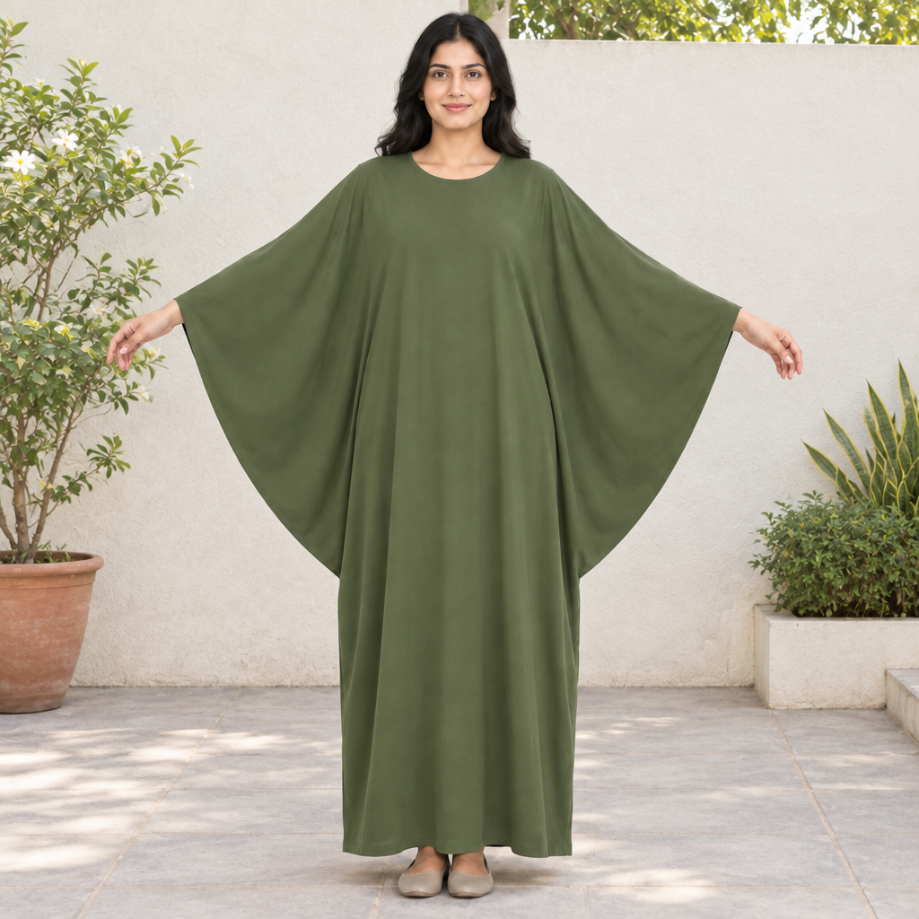 Model wearing a full-length olive batwing sleeve kaftan dress with arms extended in a sunny courtyard
