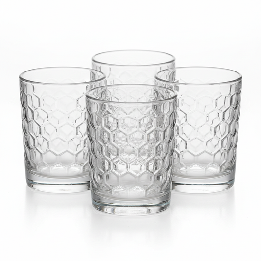 Four identical clear glass hotel juice tumblers approximately 200ml each with distinctive hexagonal geometric embossed pattern covering entire exterior surface short compact shape thick stable base arranged in cluster on white background with beautiful light refraction through embossed facets, commercial hospitality breakfast buffet glassware