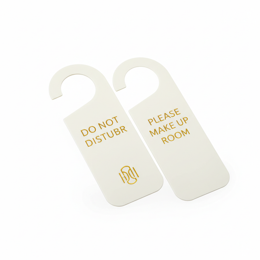 Premium ivory white PVC hotel do not disturb door hanger with die-cut door handle slot showing DO NOT DISTURB in gold foil sans-serif lettering with hotel logo emblem on front and PLEASE MAKE UP ROOM on back, smooth matte surface with rounded corners on white background