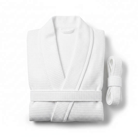 White waffle-weave hotel bathrobe folded flat showing honeycomb waffle texture across fabric surface with shawl collar and belt ties on white background, lightweight breathable warm-climate commercial hospitality spa robe