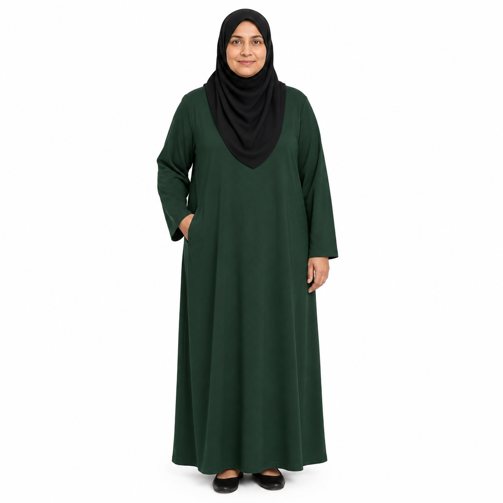 Mature model in a black hijab wearing a dark green full-length solid abaya with one hand in the side pocket, on a white background