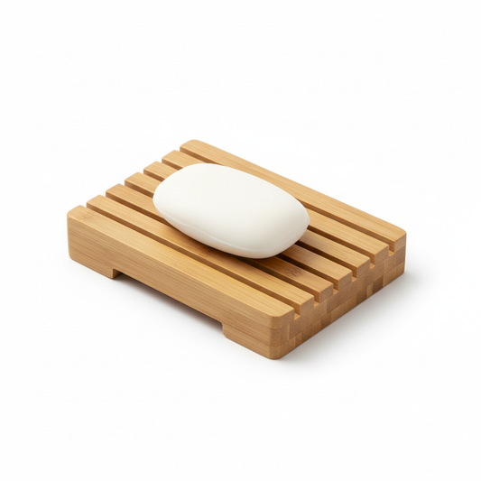 Natural bamboo hotel soap dish with drainage slats and white bar soap on white background, eco-friendly guest bathroom accessory showing grain texture and drainage design