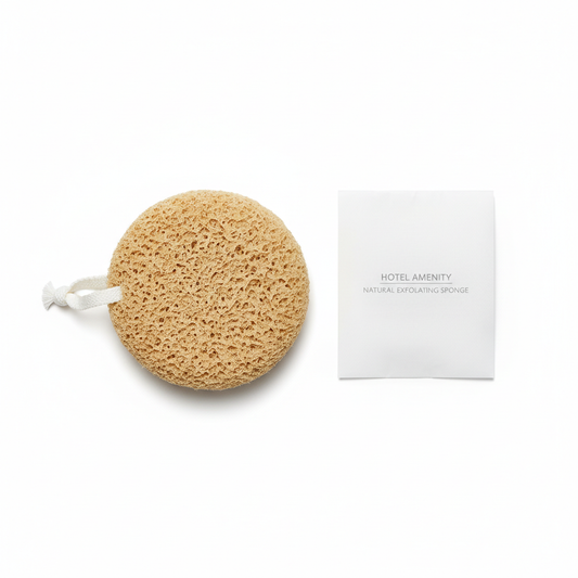 Round beige natural fiber hotel bath sponge with white hanging loop beside individual packaging sleeve on white background, guest bathroom shower amenity