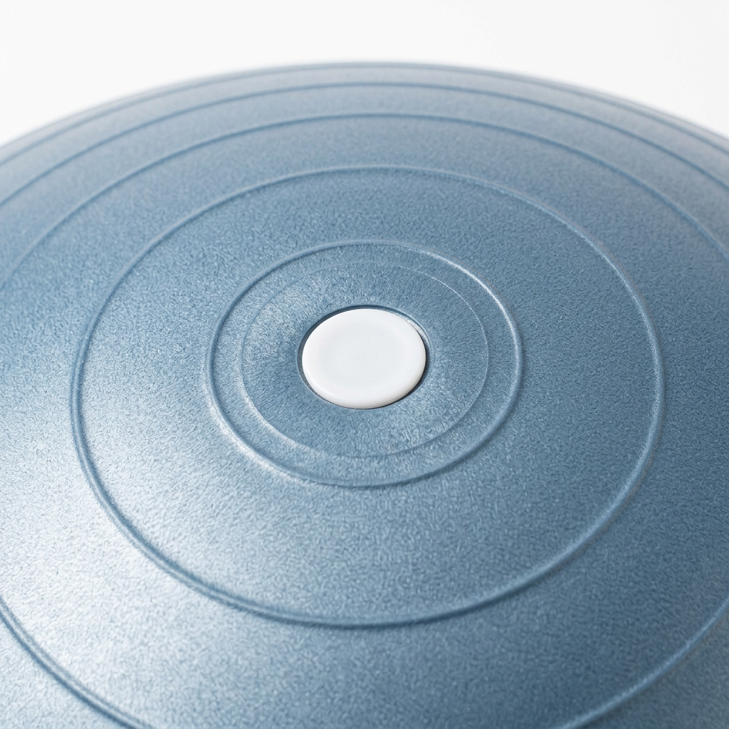 Detail close-up of inflatable exercise ball recessed valve, air plug, and concentric ribbed texture on white background