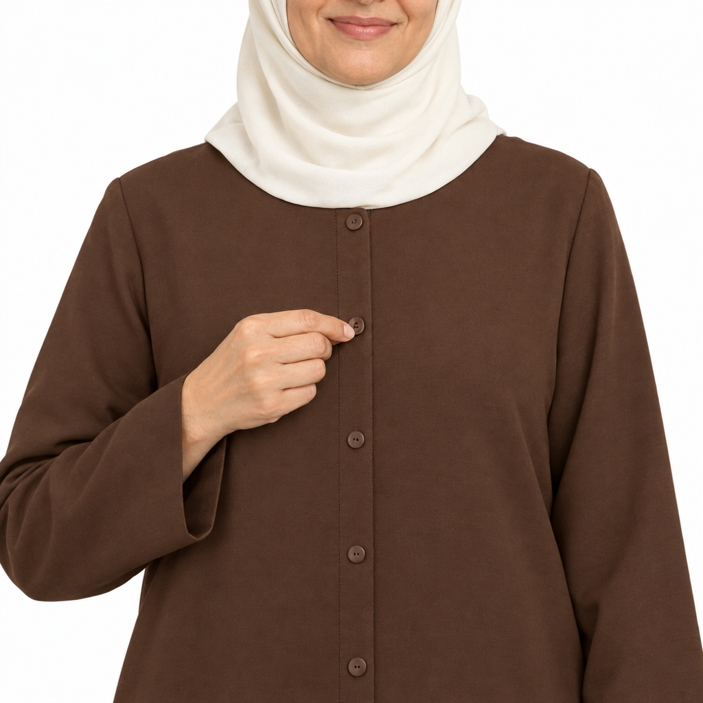 Close-up of a hand fastening a small brown button on the center front placket of a chocolate brown abaya