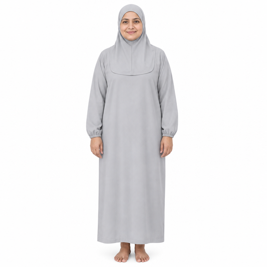 Model standing in a light grey one-piece loose prayer dress with short attached head covering and full-length straight body on a white background