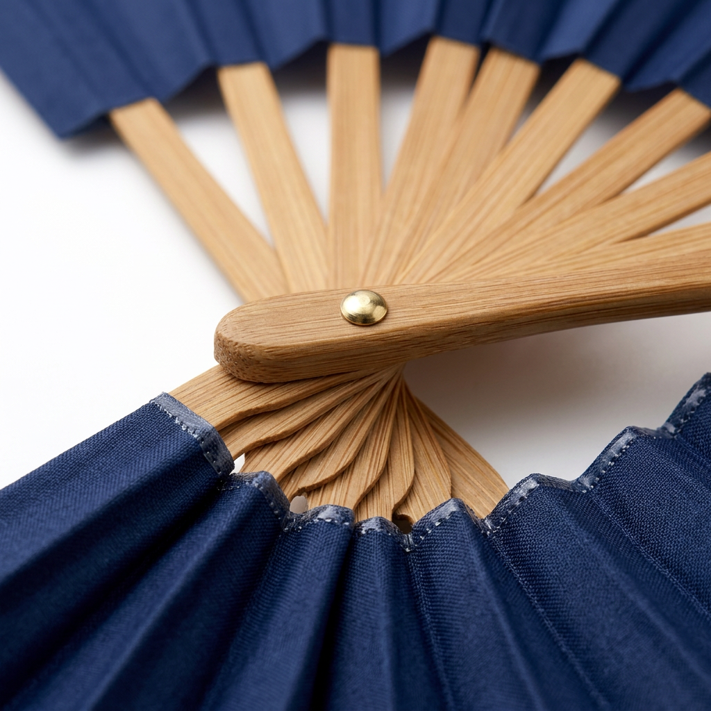 Detail close-up of promotional folding hand fan showing brass pivot pin, polished bamboo ribs, and pleated polyester fabric on white background